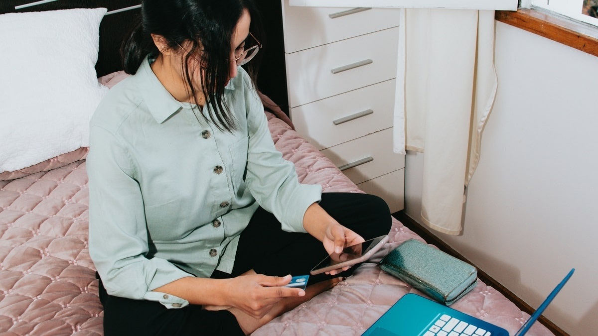 woman sitting on bed with laptop and phone