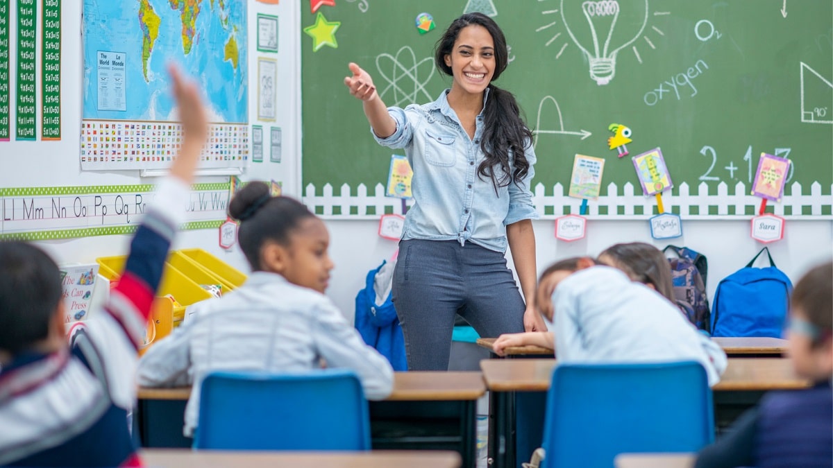 elementary school teacher smiling in classroom full of students