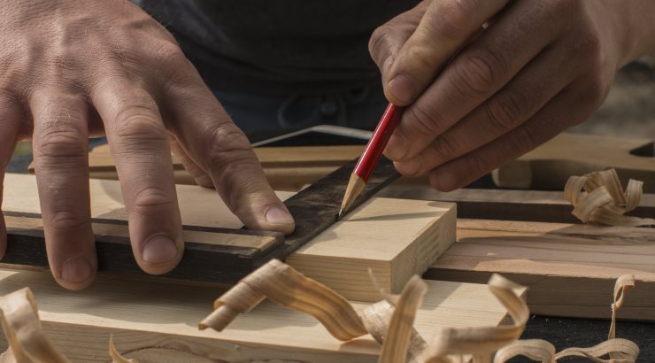 the carpenter marks with a red pencil a plank of pine with a square