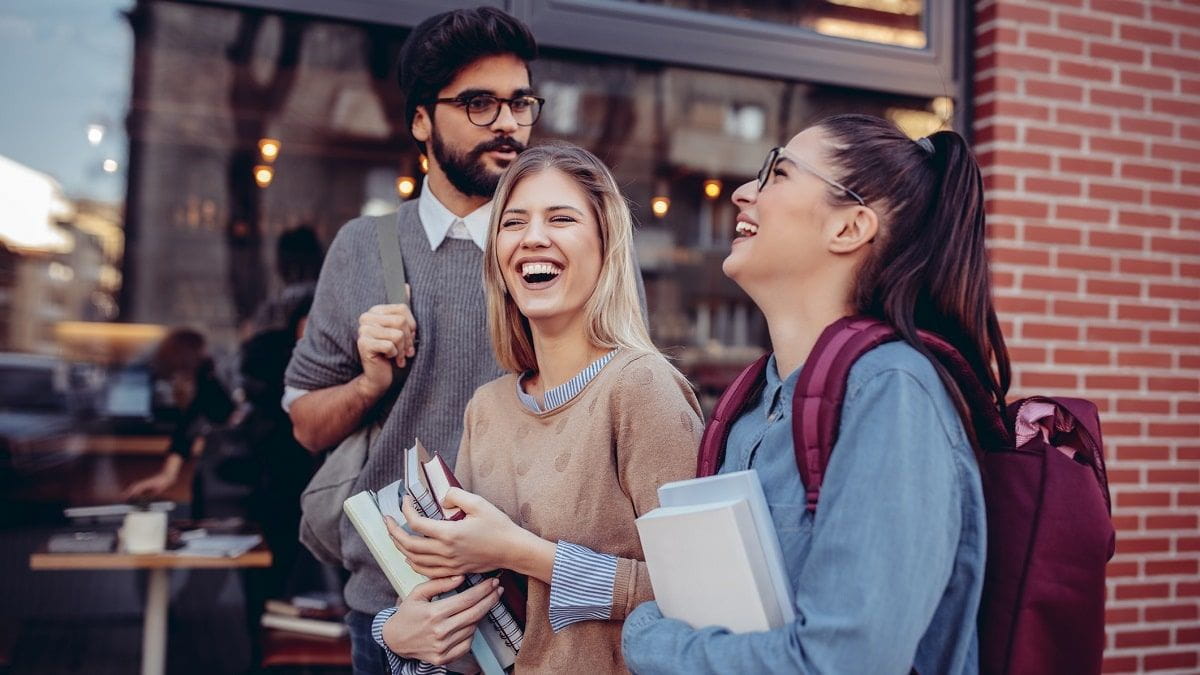college students holding books and laughing