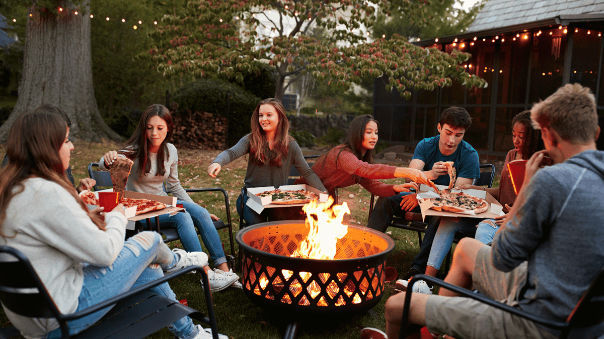 college students eating pizza around a fire