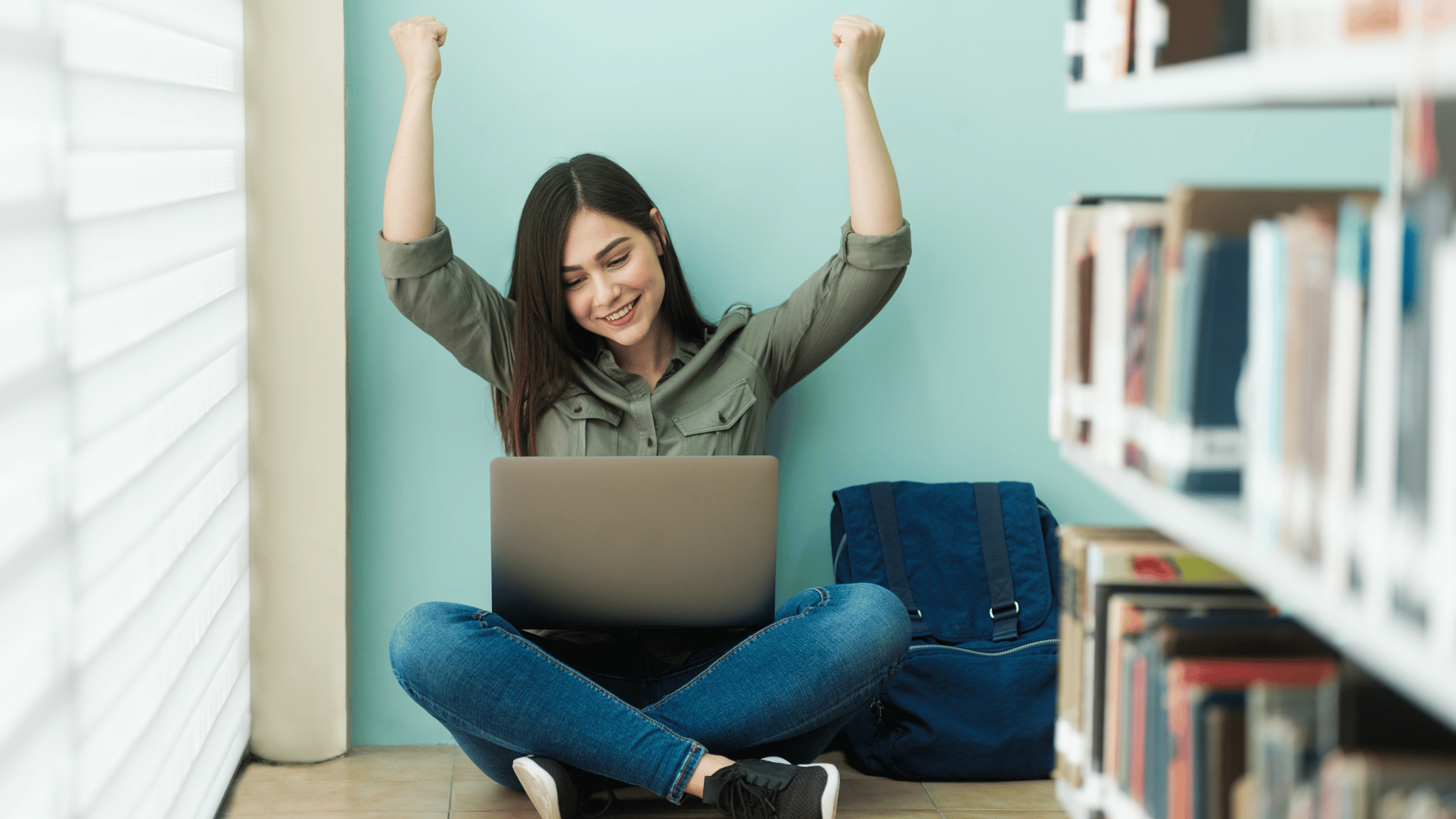 cheering female student sitting on floor in library