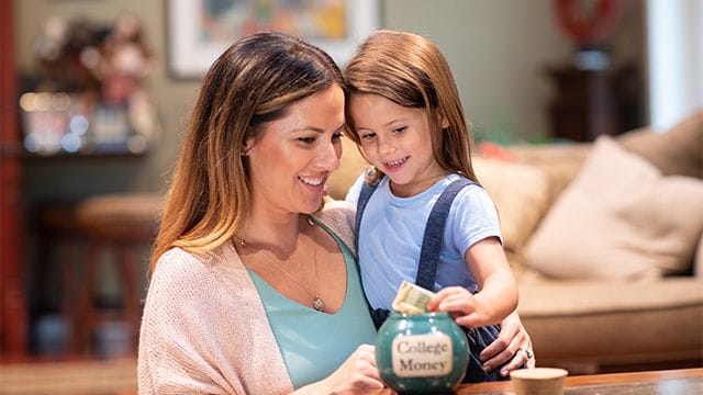 Parent and kindergartner put cash into jar marked for college savings.