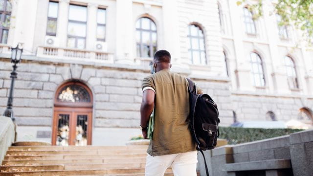 Masked student climbs steps to campus building
