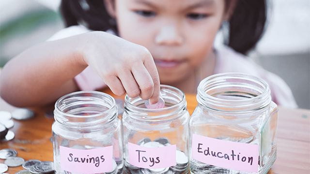Young child saves money in jars marked for separate goals.